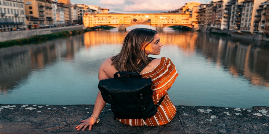 Scenic view of the Arno River with a serene lady sitting on its bank, enjoying the tranquil waters and picturesque surroundings