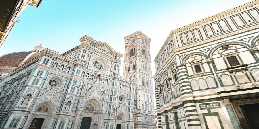Aerial view of the Cathedral of Santa Maria del Fiore, showcasing its iconic red-tiled dome and intricate marble facade, nestled among historic buildings in Florence, Tuscany, Italy.