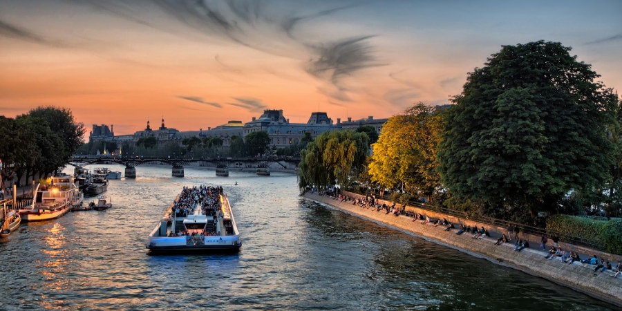 Serene Seine River scene: cruise ship glides beneath a pink sky, offering a picturesque Parisian moment along its tranquil waters.