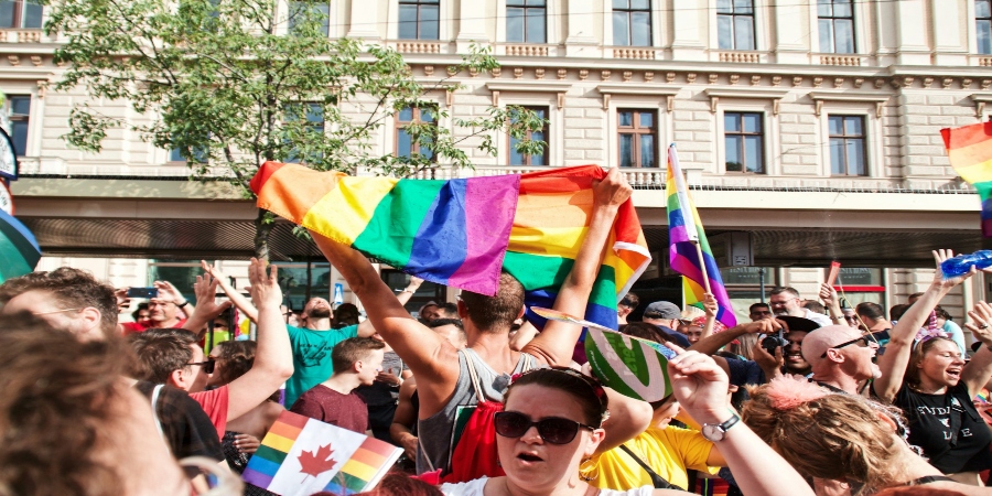 A lively crowd of people celebrating at a gay pride event. The scene is filled with vibrant colors, including rainbow flags, banners, and clothing.