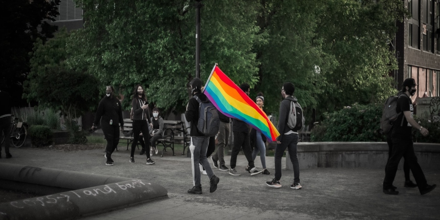A guy in Seattle holding a rainbow flag, walking through the streets and showcasing LGBTQI+ support and pride during the celebration.