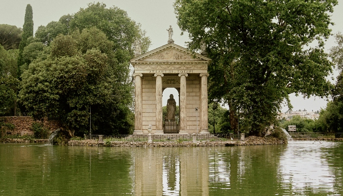statue of a lady near the lake surrounded by green trees.
