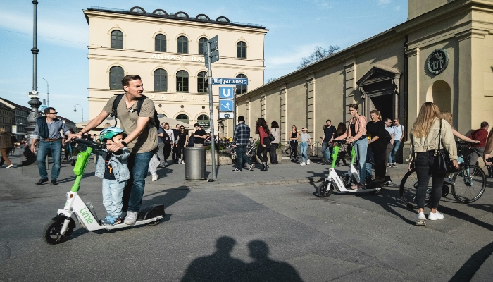 Locals and visitors riding e-scooters past Hofgarten station, capturing city life during 24 hours in Munich.