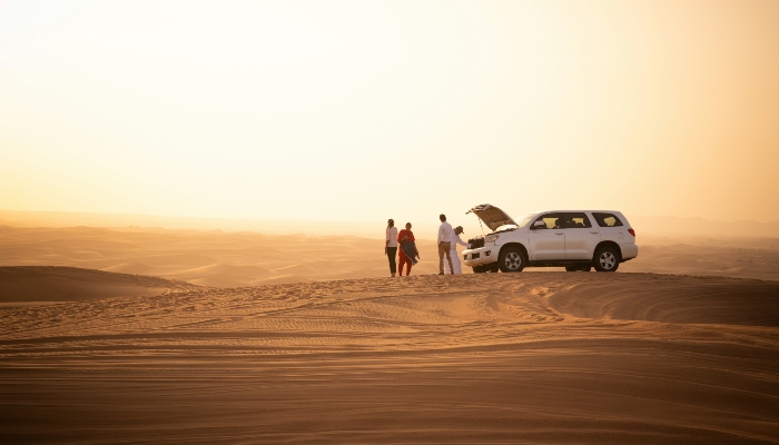 Tourists and guide beside a 4x4 vehicle in desert sunlight, exploring remote landscapes on Dubai Desert Safari Tours.
