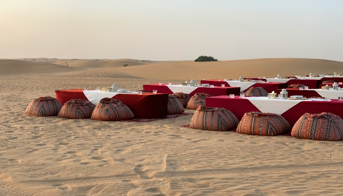 Traditional Arabian-style dinner setup on sand with dim seating and tables, showcasing authentic dining during a Dubai desert safari.
