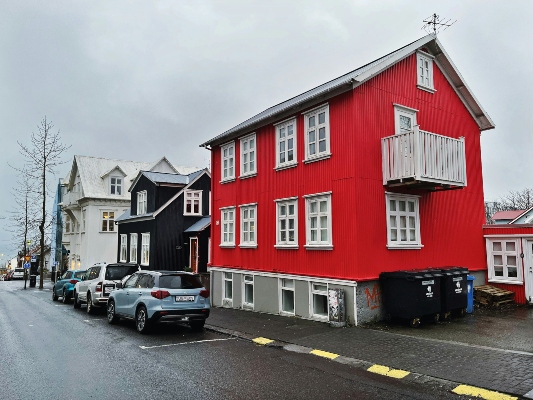 A row of colorful Scandinavian houses on a wet street in Reykjavik under an overcast sky. A vibrant red house stands out next to a black one. This charming architecture is a highlight when touring the city with Reykjavik’s hop on hop off bus.