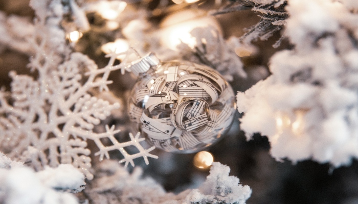 Glass ornament decorated with musical notes hangs on a snowy Christmas tree, representing festive decor found in christmas holiday destinations europe.