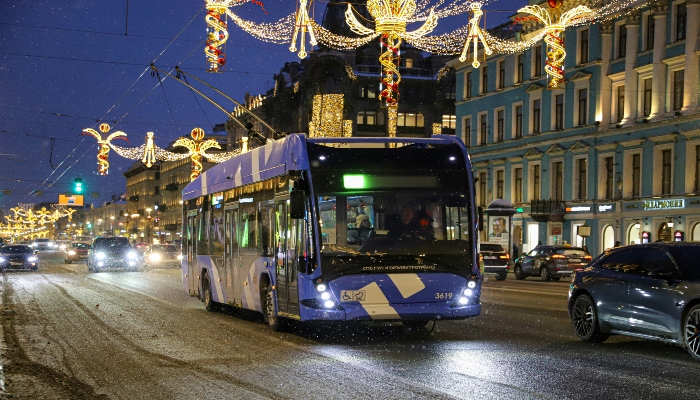 Electric city bus drives down a snow-covered street lined with holiday lights, illustrating winter travel convenience in christmas holiday destinations europe.