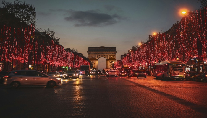 Champs-Élysées in Paris lined with dazzling red Christmas lights and the Arc de Triomphe in the distance, creating a vibrant holiday atmosphere.