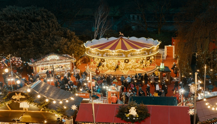 Colorful carousel surrounded by market stalls and crowds at a European Christmas fair, showing family fun and seasonal celebration in a winter destination.