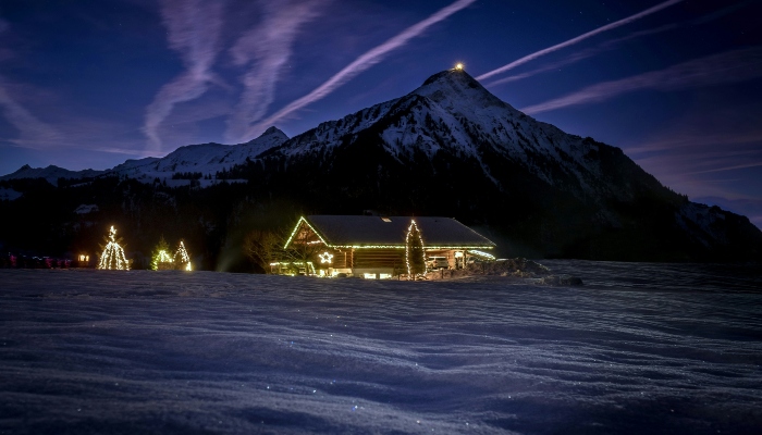 Cozy alpine cabin with twinkling Christmas trees against snow-covered mountains, representing romantic winter getaways in Europe.