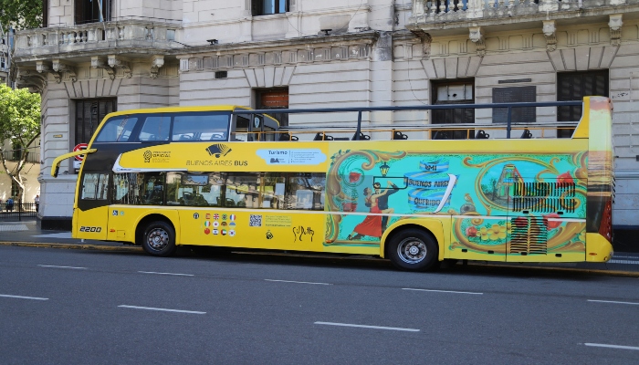 Yellow double-decker Buenos Aires tourist bus passing elegant historic buildings on a central avenue, ideal for first-time visitors exploring the city.