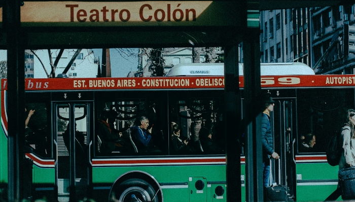 Crowded green city bus stopping at Teatro Colón in downtown Buenos Aires, showing local transport as an alternative to the Buenos Aires tourist bus.