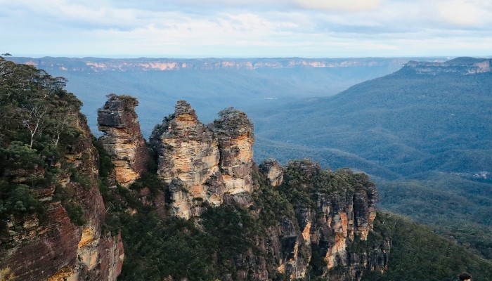 Iconic Three Sisters rock pillars rising above a forested valley on one of the best hikes near Sydney Australia in the Blue Mountains.