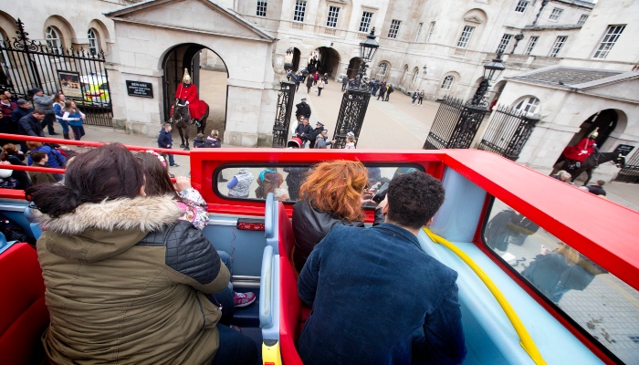 Tourists seated on an open-top bus viewing Horse Guards Parade, highlighting guided sightseeing bus tours in central London.