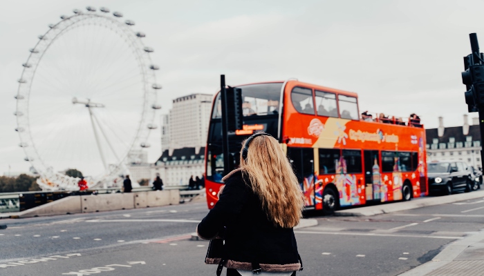 A hop-on hop-off sightseeing bus near the London Eye with pedestrians crossing the street in the foreground.