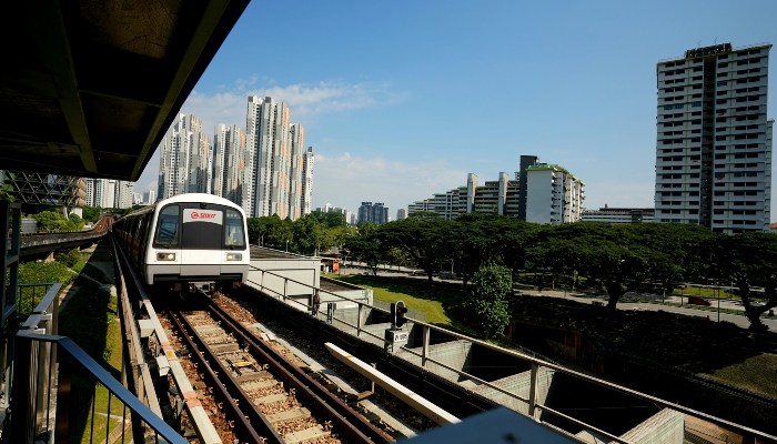 Singapore MRT train arriving at elevated station with residential towers and green spaces, contrasting public transport options discussed alongside the Singapore sightseeing bus comparison guide.