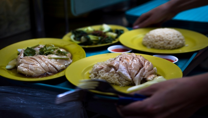 Close-up plates of Hainanese chicken rice and vegetables at a hawker centre, highlighting local food stops to pair with your Singapore sightseeing bus comparison guide.