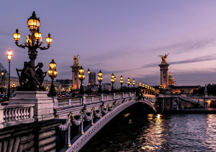 Elegant bridge over the Seine lined with ornate lampposts at dusk, showing the kind of scenic riverside vistas enjoyed during a Tootbus Paris tour.