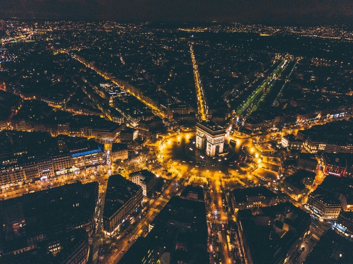 Aerial night view of the Arc de Triomphe and star-shaped avenues lit up across Paris, highlighting the grandeur seen on a Tootbus Paris tour route.