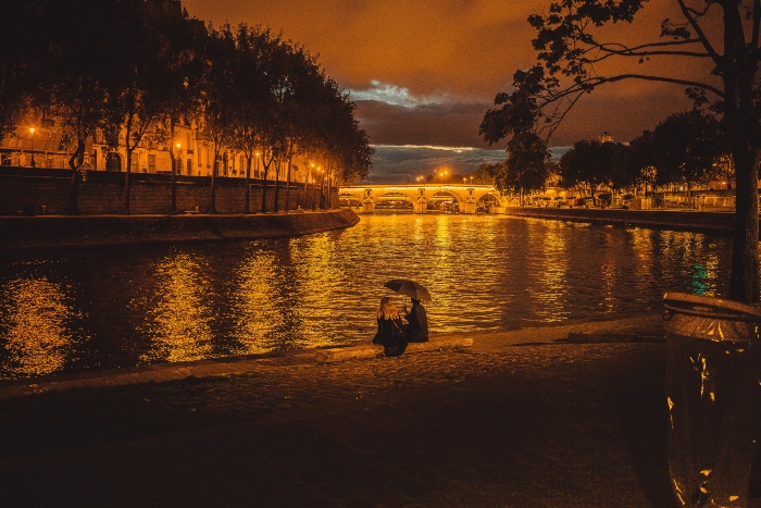 Romantic evening scene along the Seine River with warm streetlights reflecting on the water, capturing the mood of a Tootbus Paris tour at night.