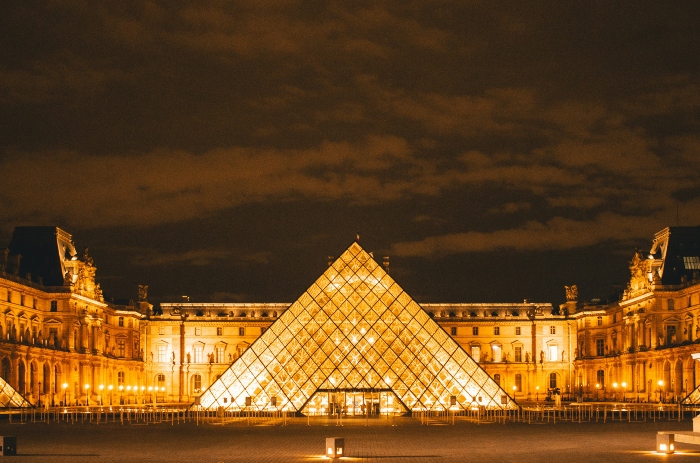 Illuminated Louvre Pyramid and palace courtyard glowing after dark, showcasing a cultural stop you can pair with a Tootbus Paris tour.