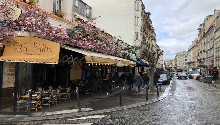 Cosy Montmartre street with café terraces, flowers, and cobblestone pavements after the rain, evoking the village atmosphere you can explore before or after a Tootbus Paris tour.