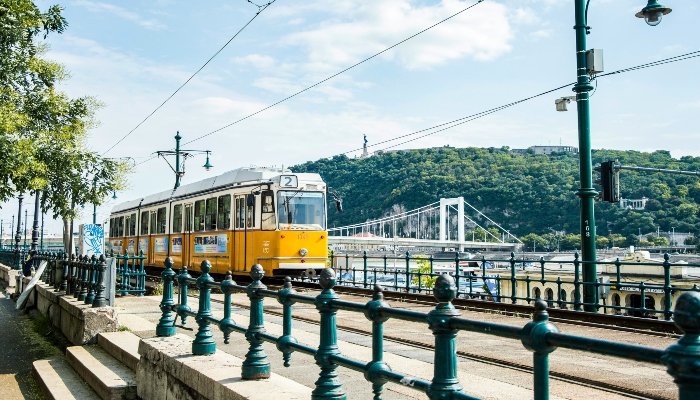 Yellow tram running along the Danube promenade in Budapest near popular sightseeing stops.