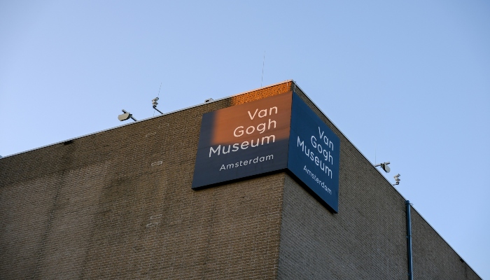 Van Gogh Museum Amsterdam sign mounted on a brick facade against a clear blue sky.