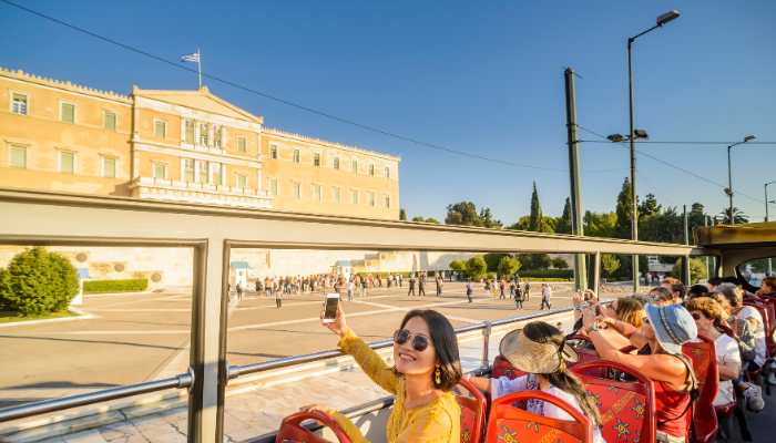 Tourist taking selfie on Athens hop-on hop-off open-top bus near Hellenic Parliament at Syntagma Square.