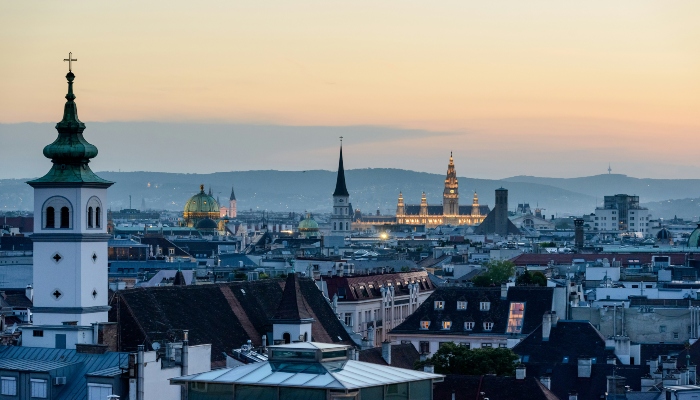 Panoramic evening view of Vienna city skyline with historic church towers and illuminated landmarks at sunset.