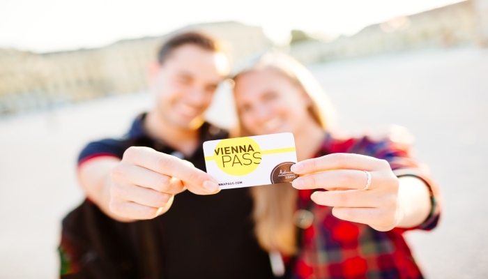 Couple holding a Vienna Pass card near the river, highlighting attraction access and sightseeing benefits.