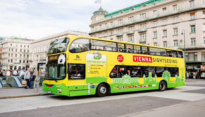 Green Vienna hop-on hop-off sightseeing bus driving through a busy historic city square.