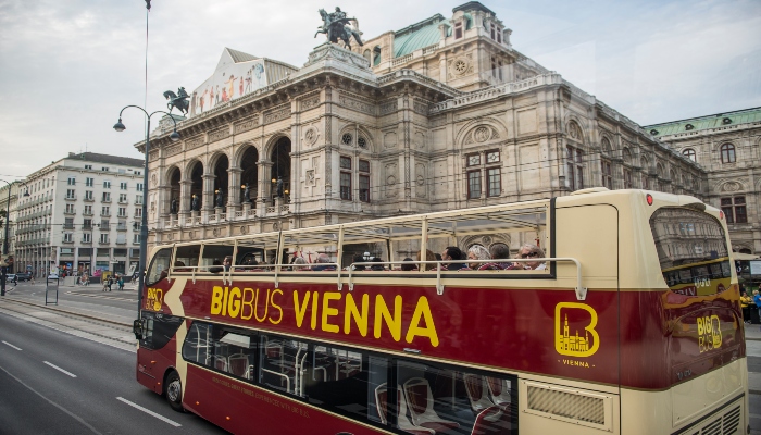 Red Big Bus Vienna sightseeing bus passing the Vienna State Opera along a main boulevard.