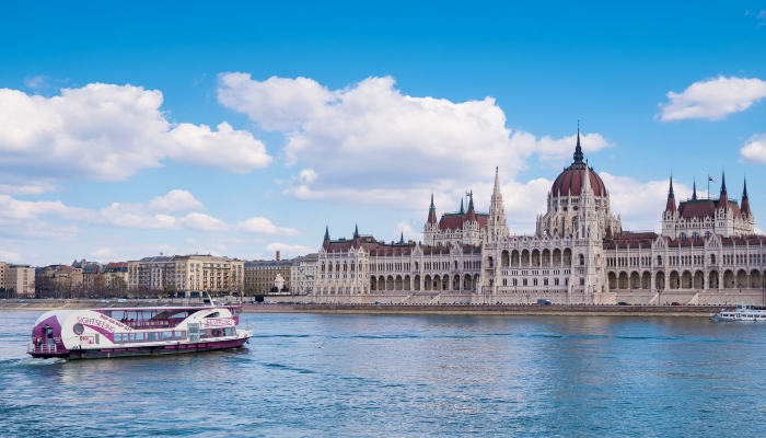 Sightseeing boat cruising on the Danube River with a grand European parliament building in the background.