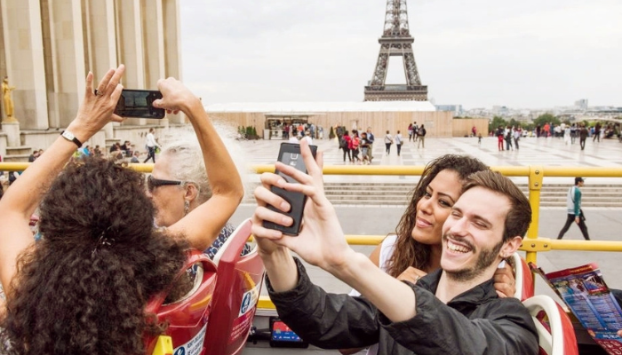 Couple taking selfies on a hop-on hop-off bus with the Eiffel Tower in the background in Paris.