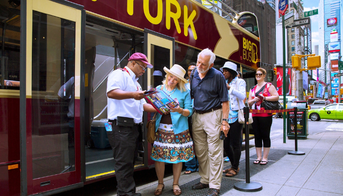 Tourists boarding a New York hop-on hop-off bus near Times Square sightseeing stop.