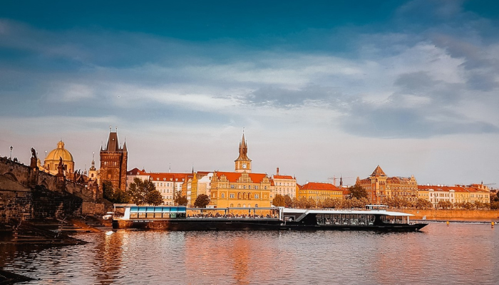 Prague skyline and Charles Bridge with a river cruise boat during spring evening.