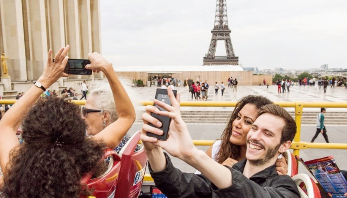 Tourists taking selfies on hop-on hop-off bus with Eiffel Tower in the background.