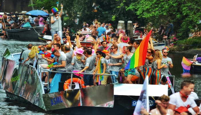 Amsterdam Pride Canal Parade boat filled with people waving rainbow flags during canal celebrations.