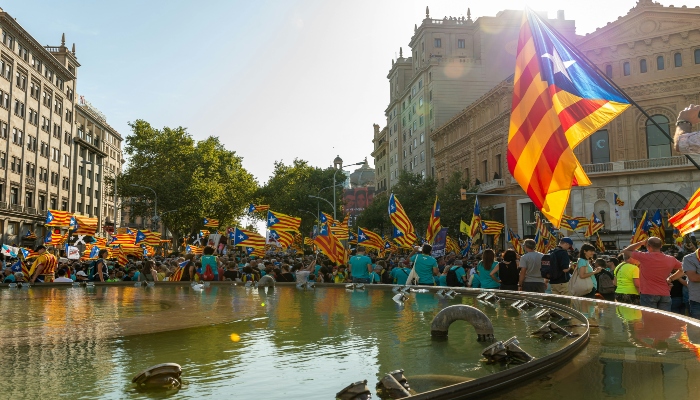 Pride Barcelona celebration crowd gathered near city square fountain with rainbow flags during daytime event.