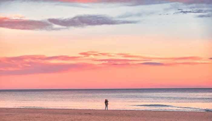 A person standing on a quiet Spanish beach at sunset, romantic seaside moment ideal for honeymooners in Spain.