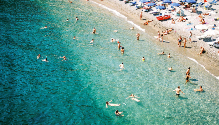 People enjoying sunbathing and swimming in the water along the Amalfi Coast overlooking the Mediterranean Sea in Italy.