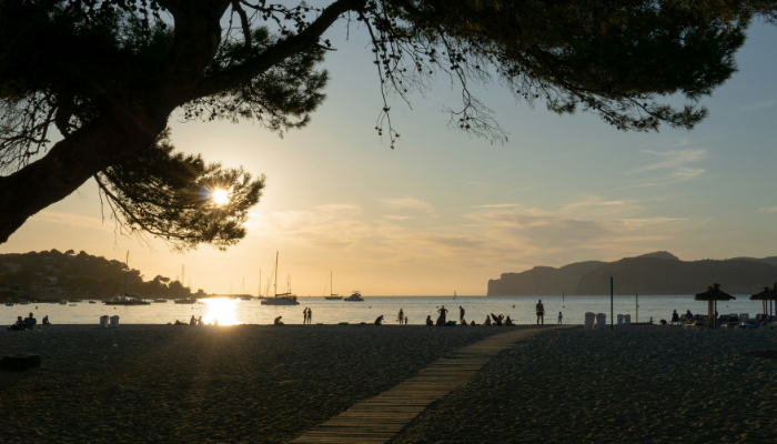 Golden sunset view at Cala Mondragó beach in Mallorca with boats and couples relaxing along the shore.