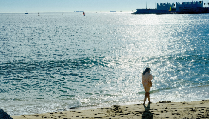 Woman walking along Barceloneta Beach in Barcelona with sparkling Mediterranean waters on a sunny day.