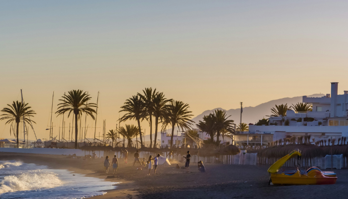 Evening beach promenade with palm trees and seaside cafés in Marbella, a romantic coastal destination in Spain.