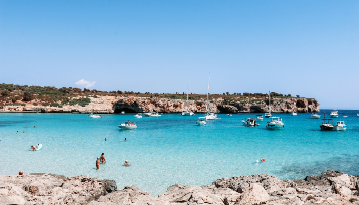 Turquoise Mediterranean cove with anchored boats along Mallorca’s rocky coastline.