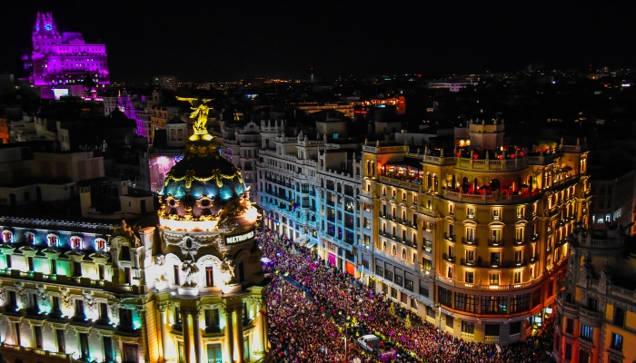 Madrid Pride celebration crowd filling Gran Vía at night with illuminated buildings and festival atmosphere.