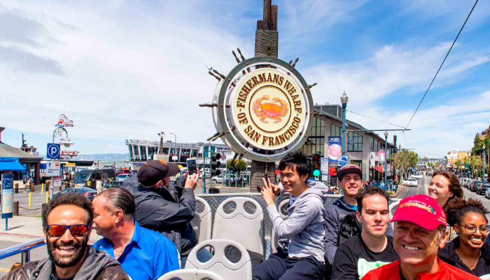 Tourists riding an open-top sightseeing bus near the Fisherman’s Wharf sign in San Francisco, a popular stop for San Francisco for first time visitors.