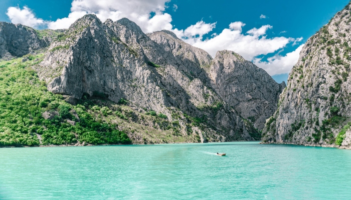 Albanian Riviera coastline with turquoise sea, rocky cliffs, and seaside houses under clear blue sky.